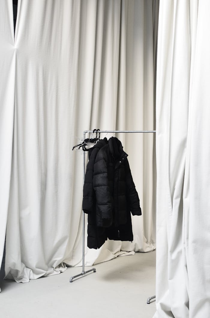 why-choose-us Black jacket hanging on a rack against white curtains in a minimalist room.