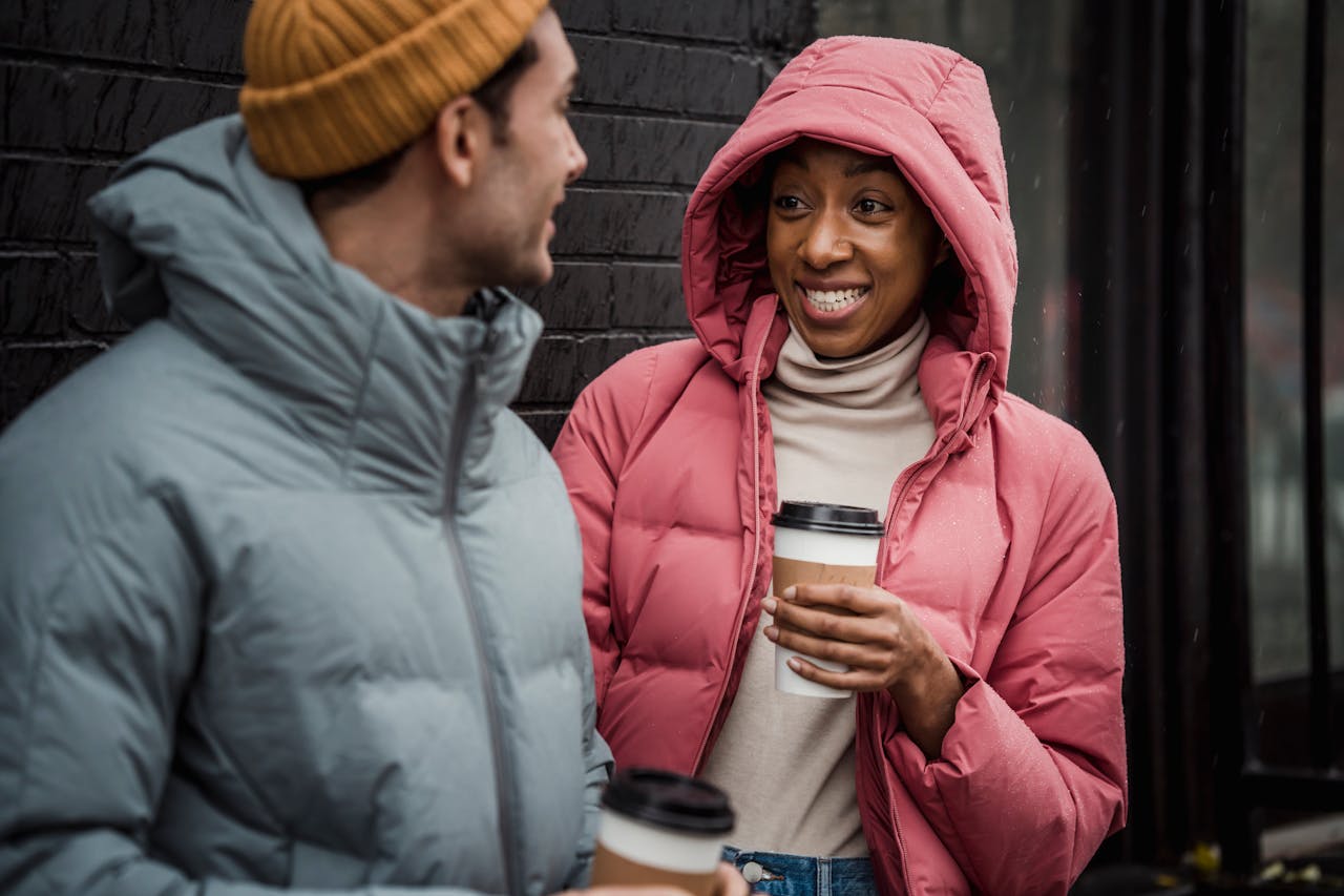 home-hero Smiling couple in winter coats enjoying hot coffee outdoors on a chilly day.